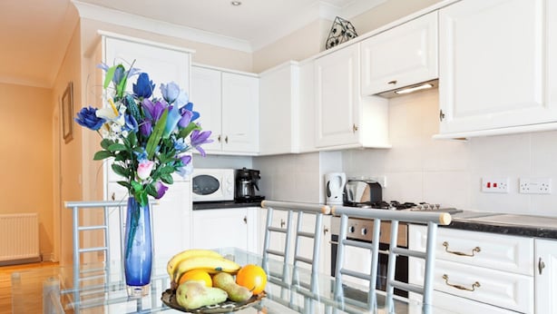 Une cuisine moderne avec des meubles blancs, une table à manger en verre et un vase rempli de fleurs.