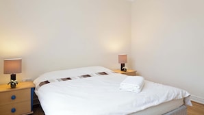 Une chambre d’hôtel avec un grand lit, deux tables de chevet et deux lampes fixées au mur.