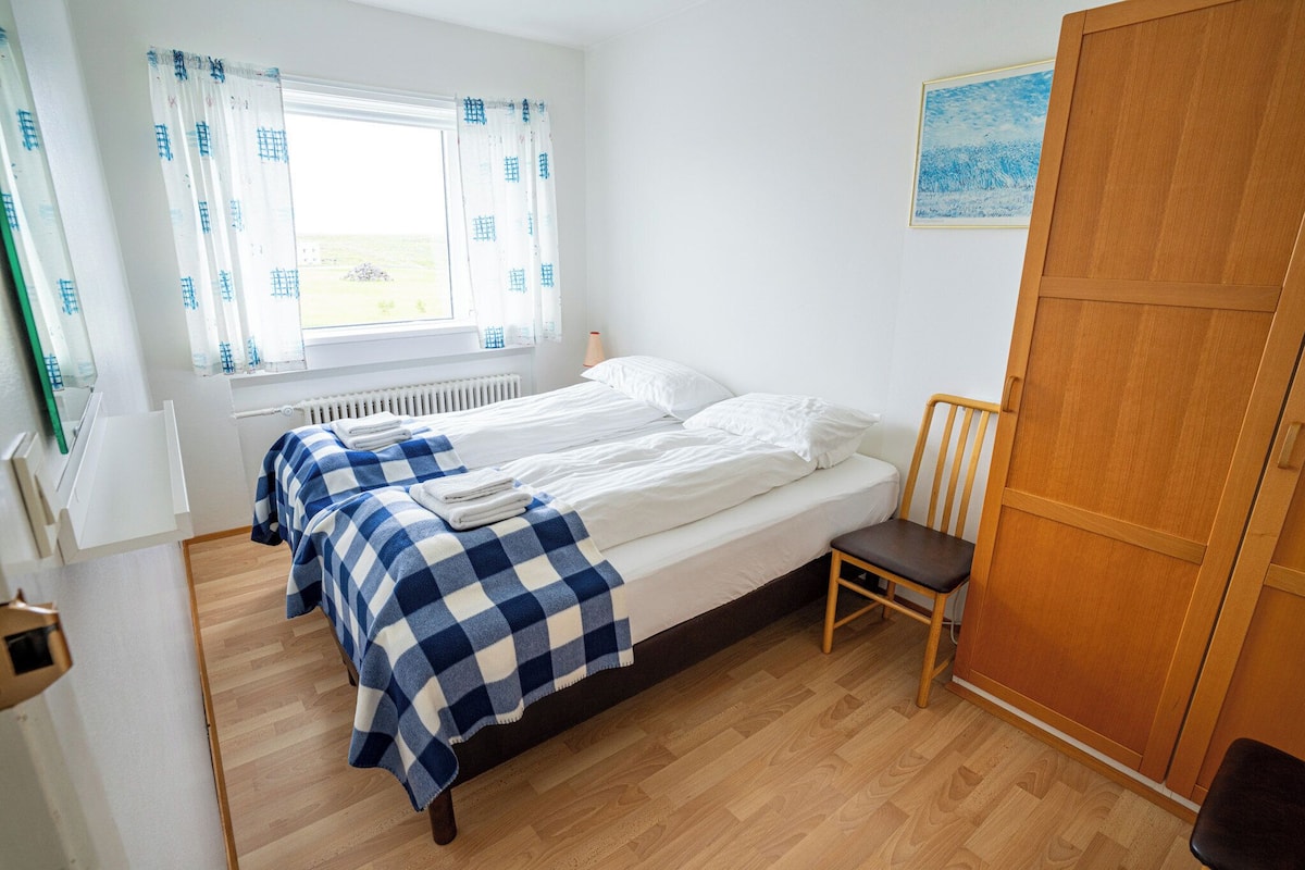A room with a bed, a chair, a radiator, a window with curtains, and a painting on the wall.