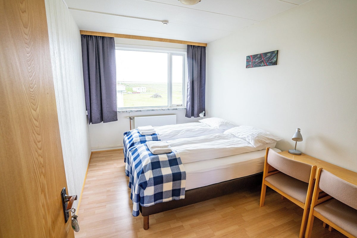 A small, tidy room with a bed, a bench, a window, and a radiator.