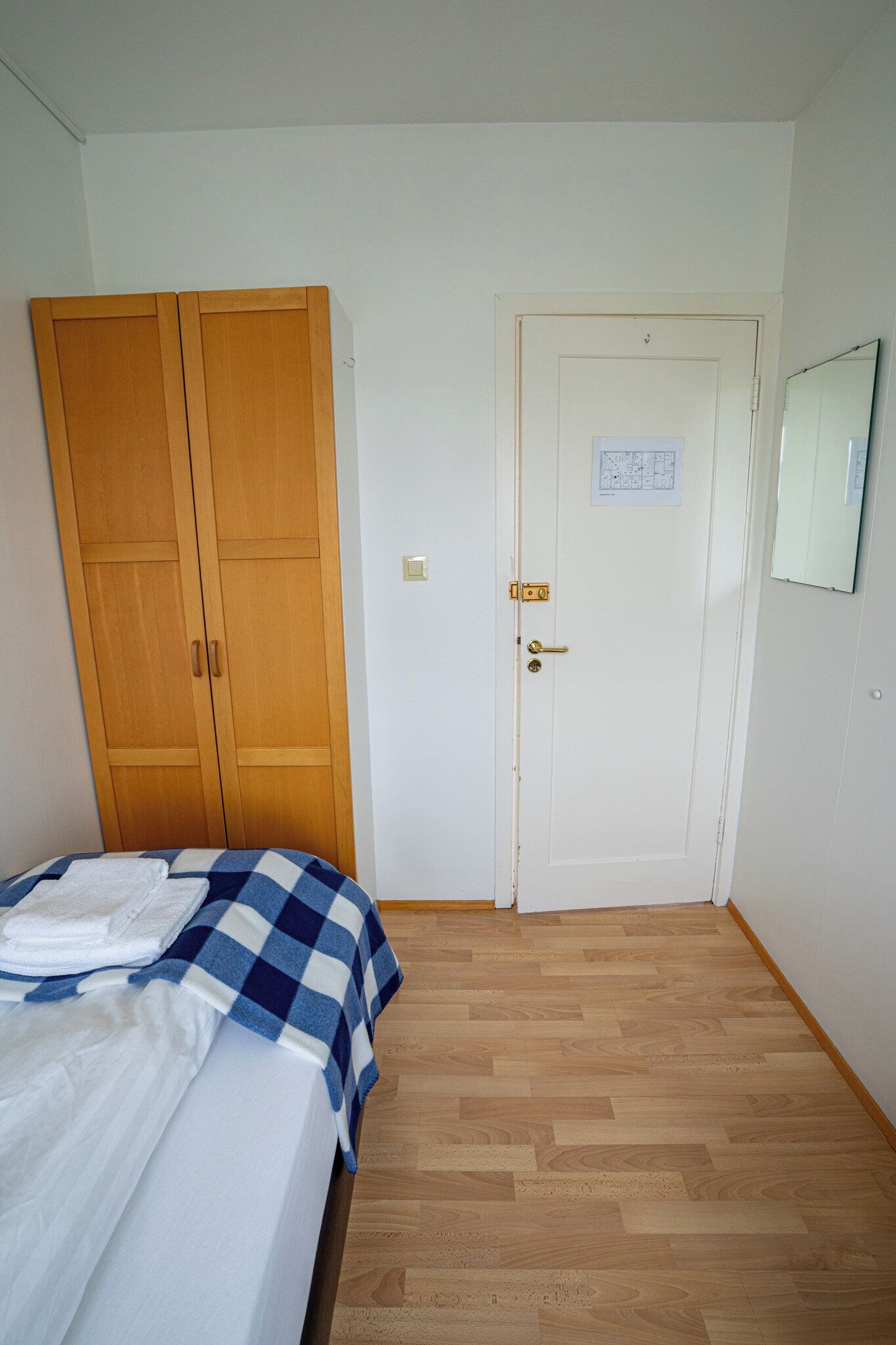 Un dormitorio con cama, armario de madera, puerta blanca y espejo en la pared.