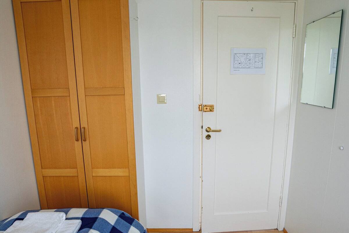A bedroom with a bed, a wooden wardrobe, a white door, and a mirror on the wall.