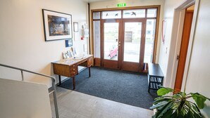 Een hotel lobby met een receptiebalie, ingelijste kunstwerken, een grote plant en een uitzicht op buiten door de glazen deuren.
