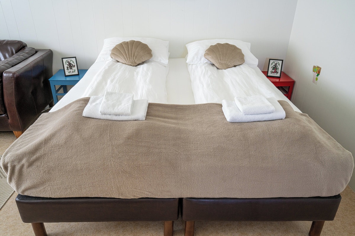 A double bed with two pillows, a brown blanket, and a small bedside table with a picture frame.