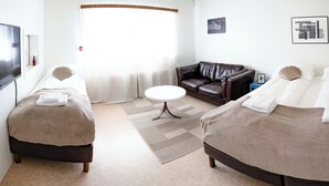 A hotel room with two beds, a sofa, a TV, and artwork on the walls. - The Nest Guesthouse (Raufarhofn)