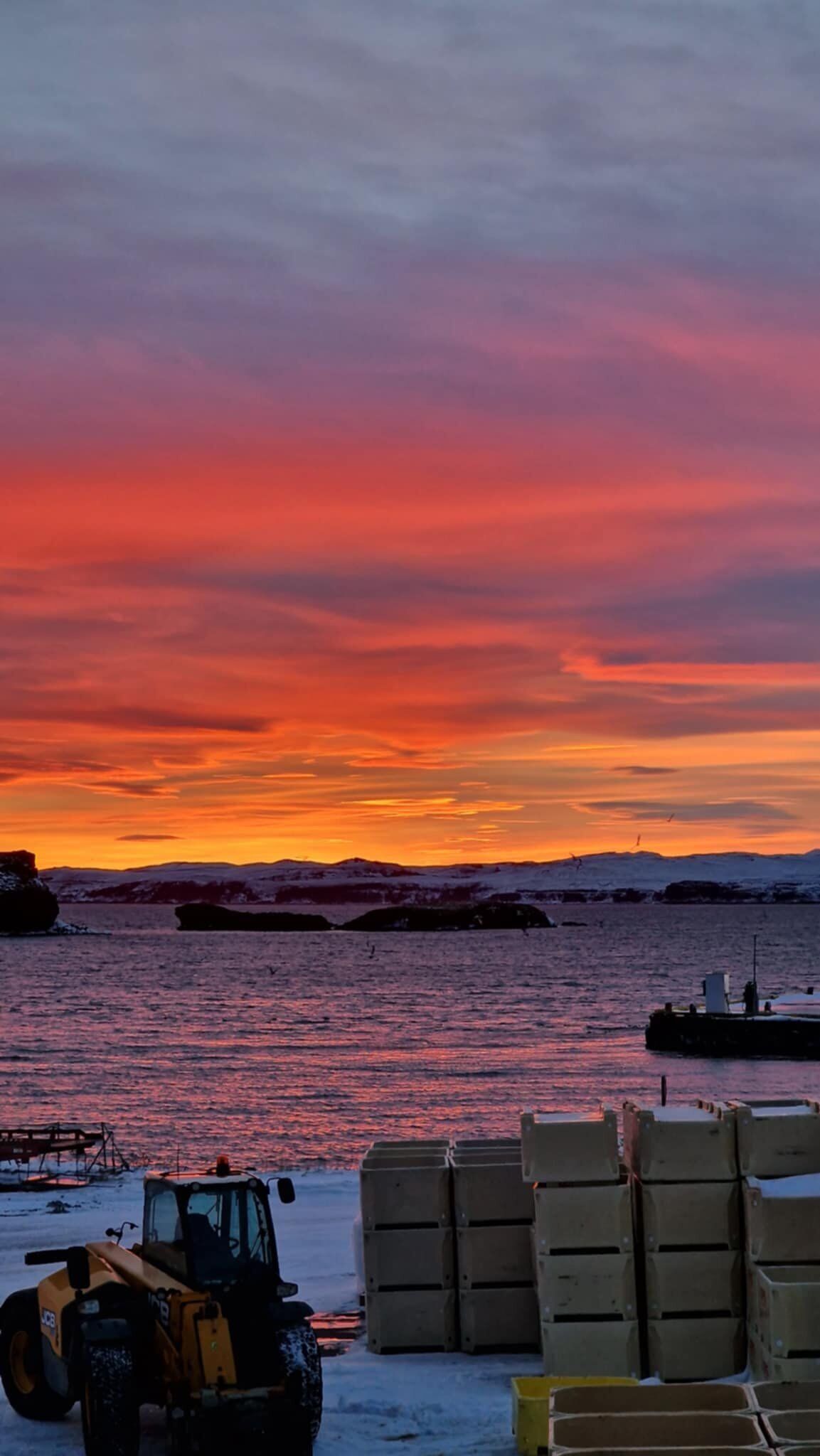 A snow-covered landscape with a sunset, a snowmobile, and stacked shipping containers.