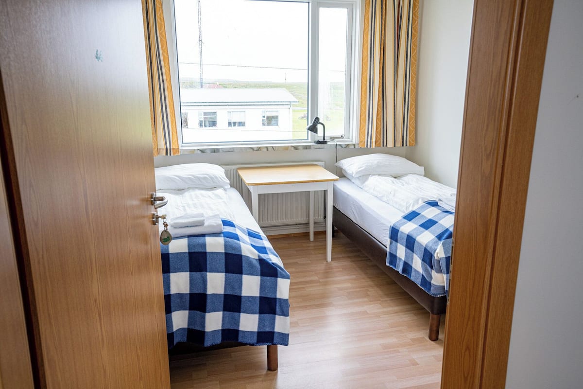 A room with two beds, a desk, and a window with curtains.