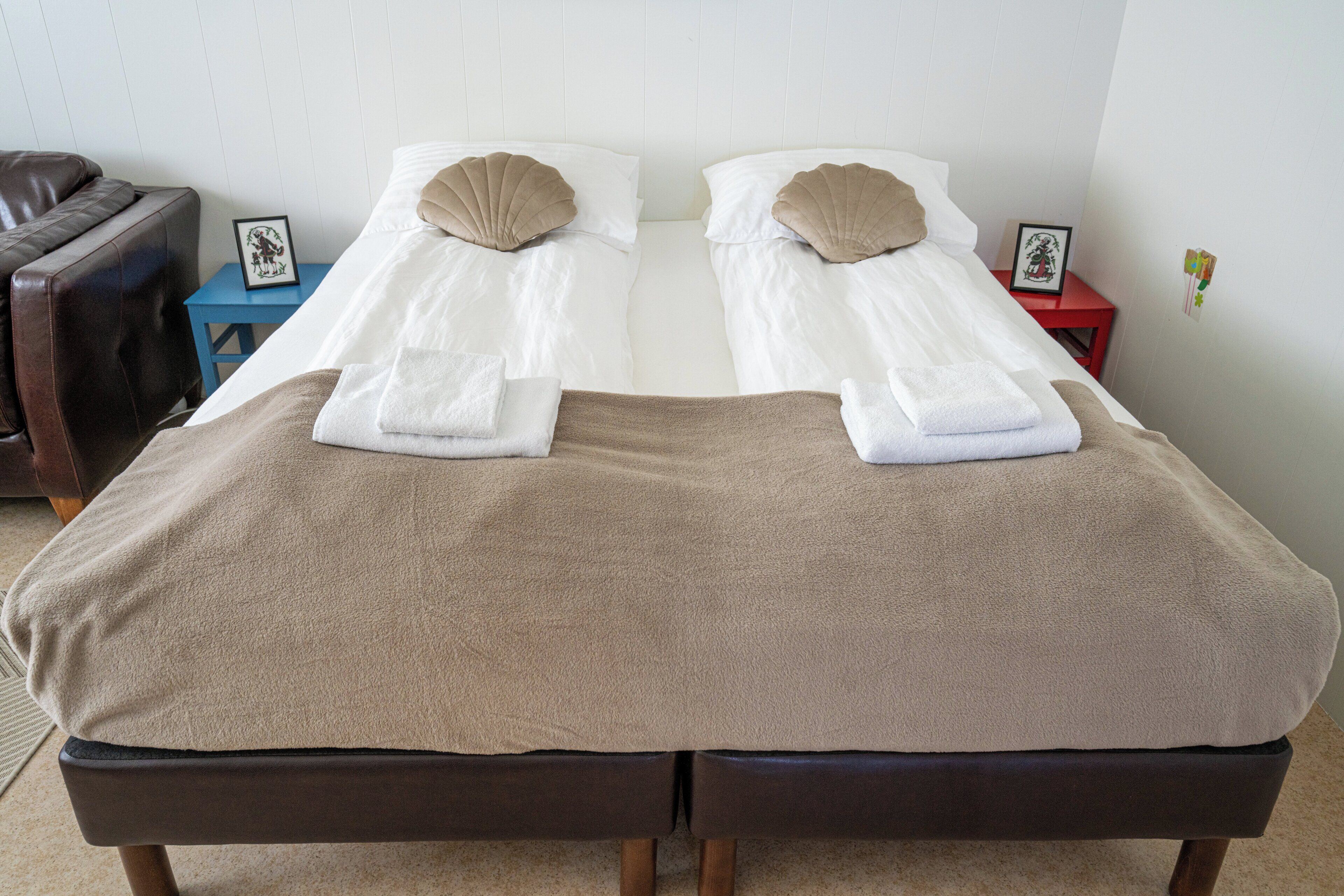 A double bed with two pillows, a brown blanket, and a small bedside table with a picture frame.