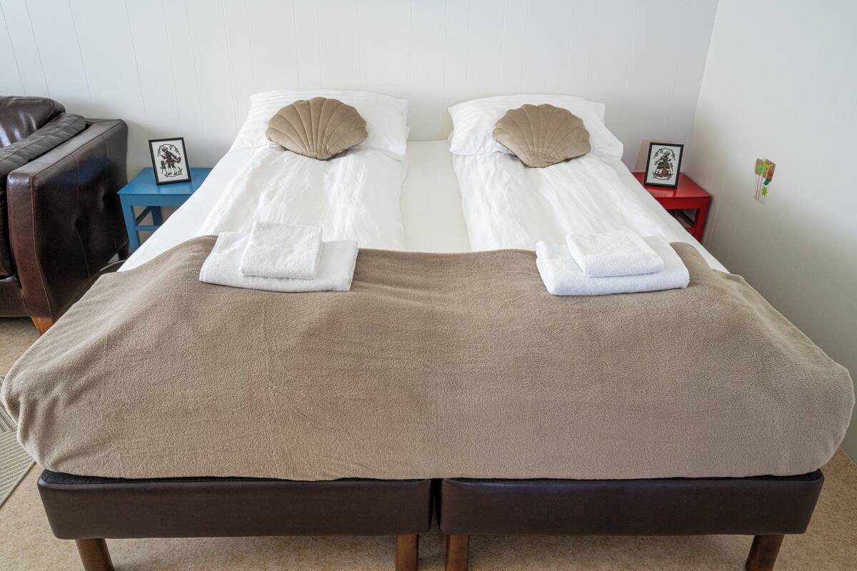 A double bed with two pillows, a brown blanket, and a small bedside table with a picture frame.