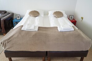 A double bed with two pillows, a brown blanket, and a small bedside table with a picture frame. - The Nest Guesthouse (Raufarhofn)