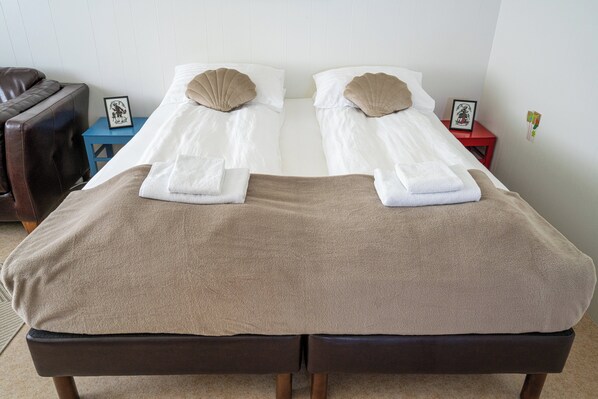 A double bed with two pillows, a brown blanket, and a small bedside table with a picture frame. - The Nest Guesthouse (Raufarhofn)