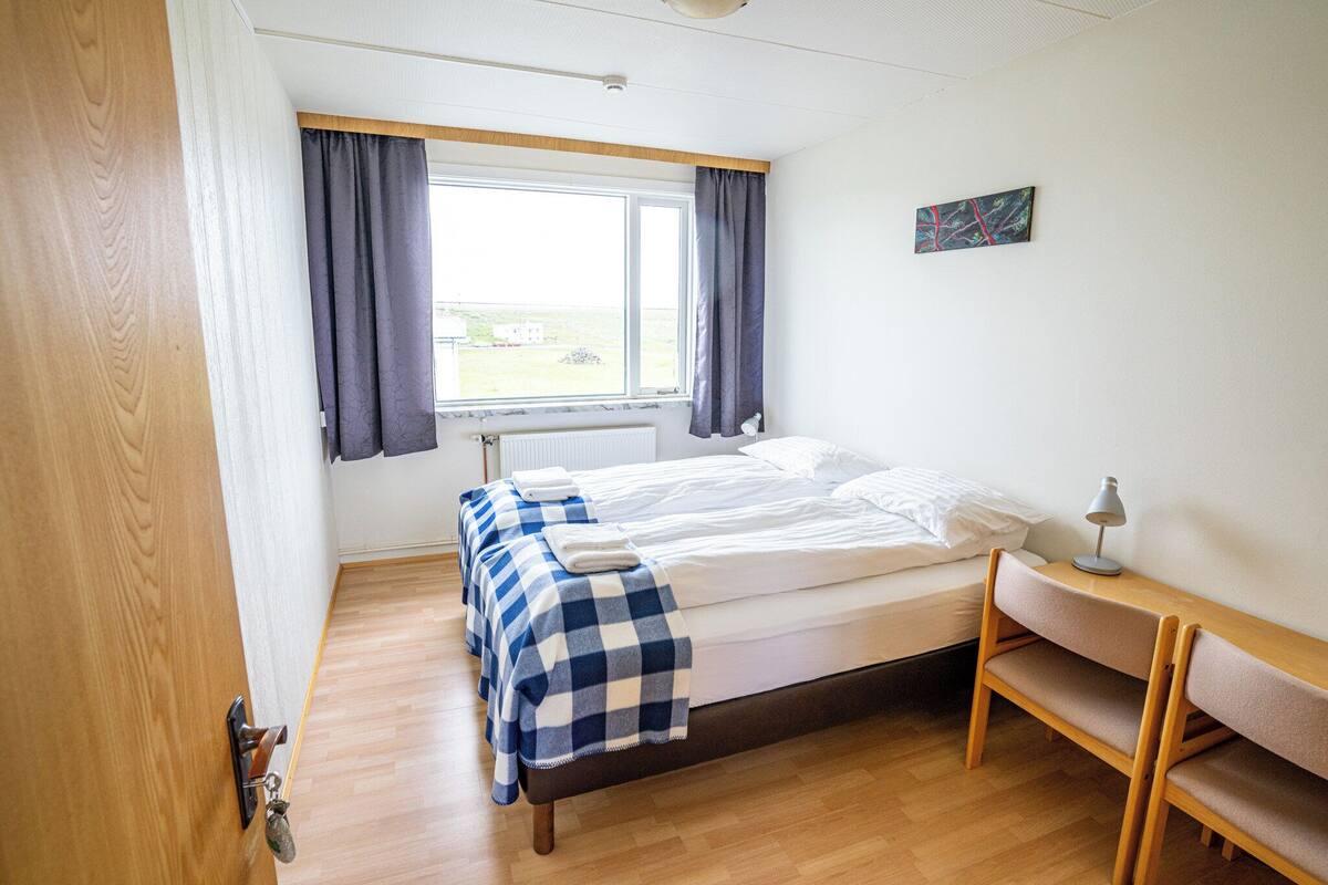 A small, tidy room with a bed, a bench, a window, and a radiator.