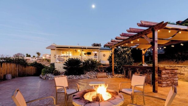 Ein Patio-Bereich mit einem Steinkamin, Sitzgelegenheiten im Freien und einer Pergola mit Lichterketten.