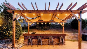 Ein Außenbereich mit Bar, einer Pergola, Steinsitzgelegenheiten und Lichterketten.