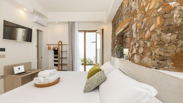 A modern hotel room with a large bed, a TV, a laptop, and a stone accent wall. - Ausentu Guest House (Tortoli)