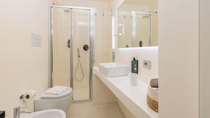 A modern bathroom with a glass-enclosed shower, a white sink, and a mirror above the sink. - Ausentu Guest House (Tortoli)