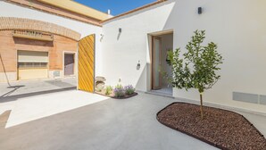A modern building with a white exterior, a wooden door, and a small garden area with plants and a tree. - Ausentu Guest House (Tortoli)