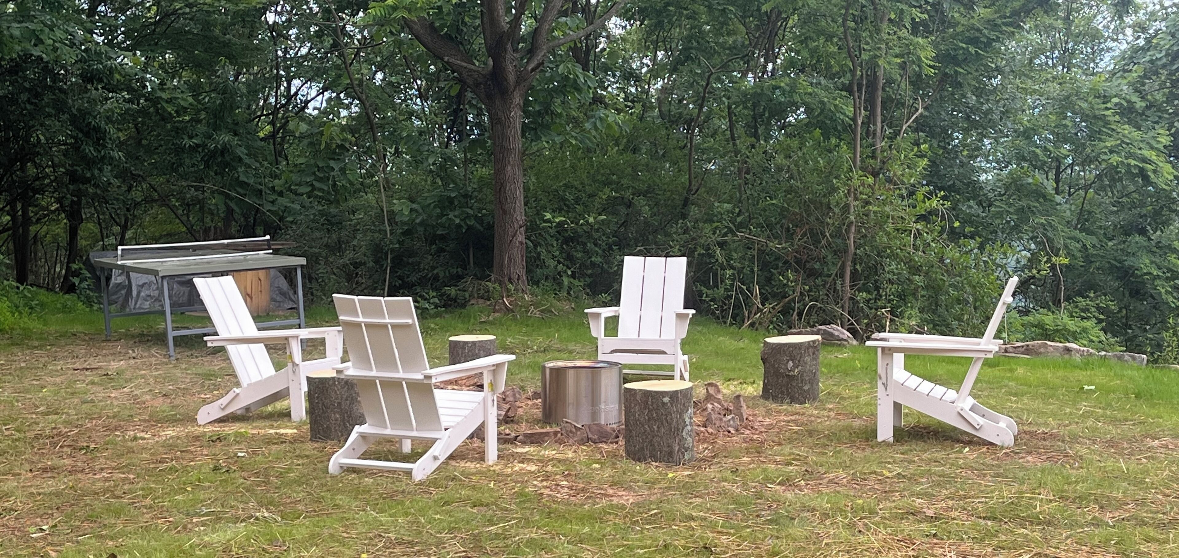 Buiten zitplaatsen met Adirondack stoelen en een tafel, omringd door bomen.