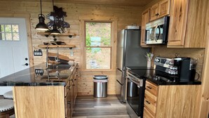 A compact kitchen with wooden cabinetry, a stainless steel refrigerator, a coffee machine, and a window providing a view of the outdoors.