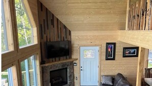 A cozy cabin interior with a stone fireplace, leather sofa, and a television mounted on the wall.
