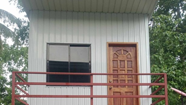 A two-story building with a balcony, a wooden door, and a small porch area with a plant. - 1 Bed House - Sleeps 2 - Parking - Wifi (Zamboanga)