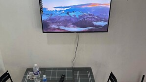 A dining area with a table, chairs, a TV mounted on the wall, and a broom in the corner. - 1 Bed House - Sleeps 2 - Parking - Wifi (Zamboanga)
