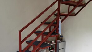 A staircase with red railings leading to a landing area with storage shelves and a refrigerator. - 1 Bed House - Sleeps 2 - Parking - Wifi (Zamboanga)
