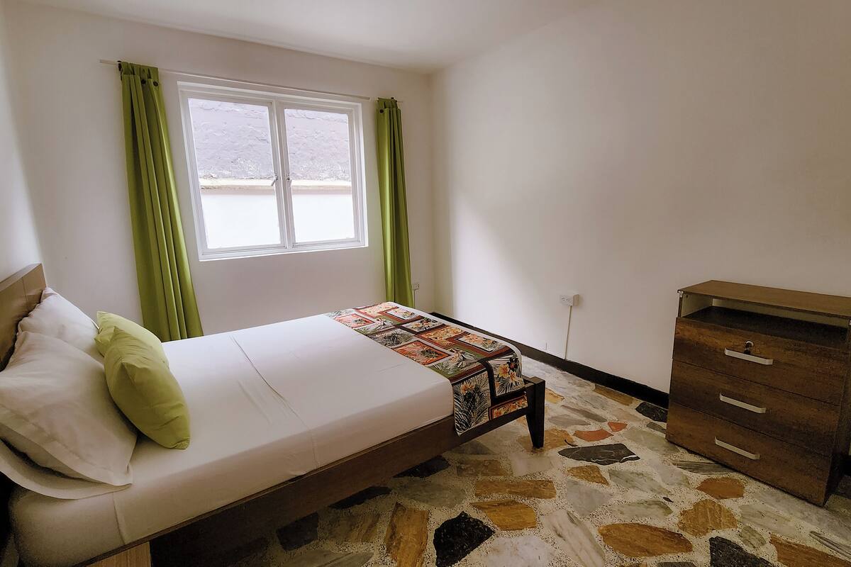 A bedroom with a bed, a dresser, a window with curtains, and a patterned rug.