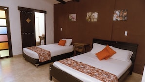A hotel room with two beds, each with a brown headboard and white bedding. There are wooden nightstands and a small table between the beds. The walls are adorned with framed artwork, and the room has a tiled floor. - Tuki Hostel & Lounge (Pereira)