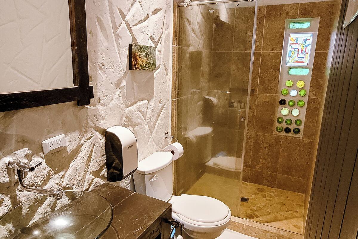 A bathroom with a glass shower enclosure, a toilet, and a sink with a glass bowl.