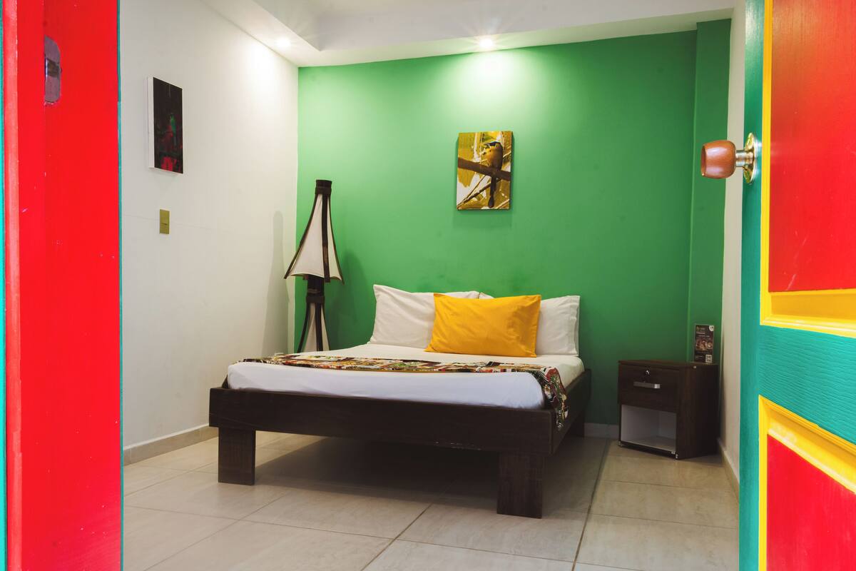A room with a bed, a nightstand, a lamp, and a green wall.