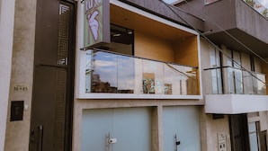 A modern building with a glass balcony, a visible door, and a sign with a logo. - Tuki Hostel & Lounge (Pereira)
