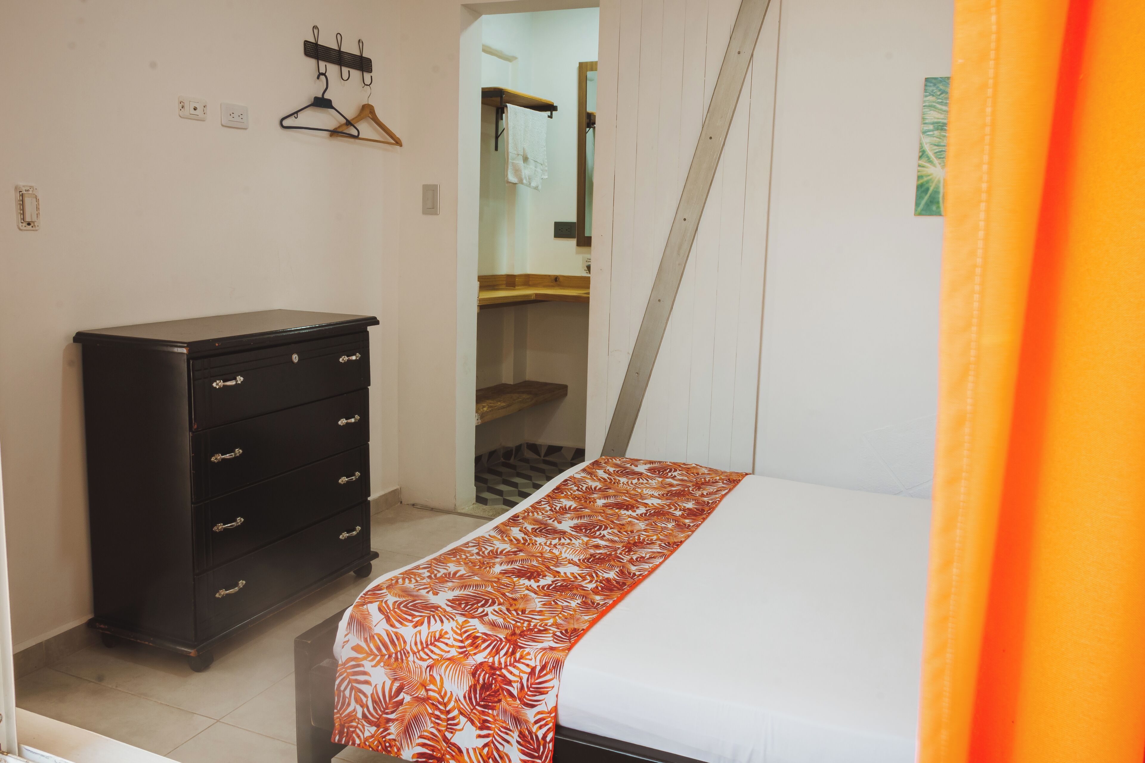 A bedroom with a bed, a dresser, a mirror, and a door leading to a bathroom.