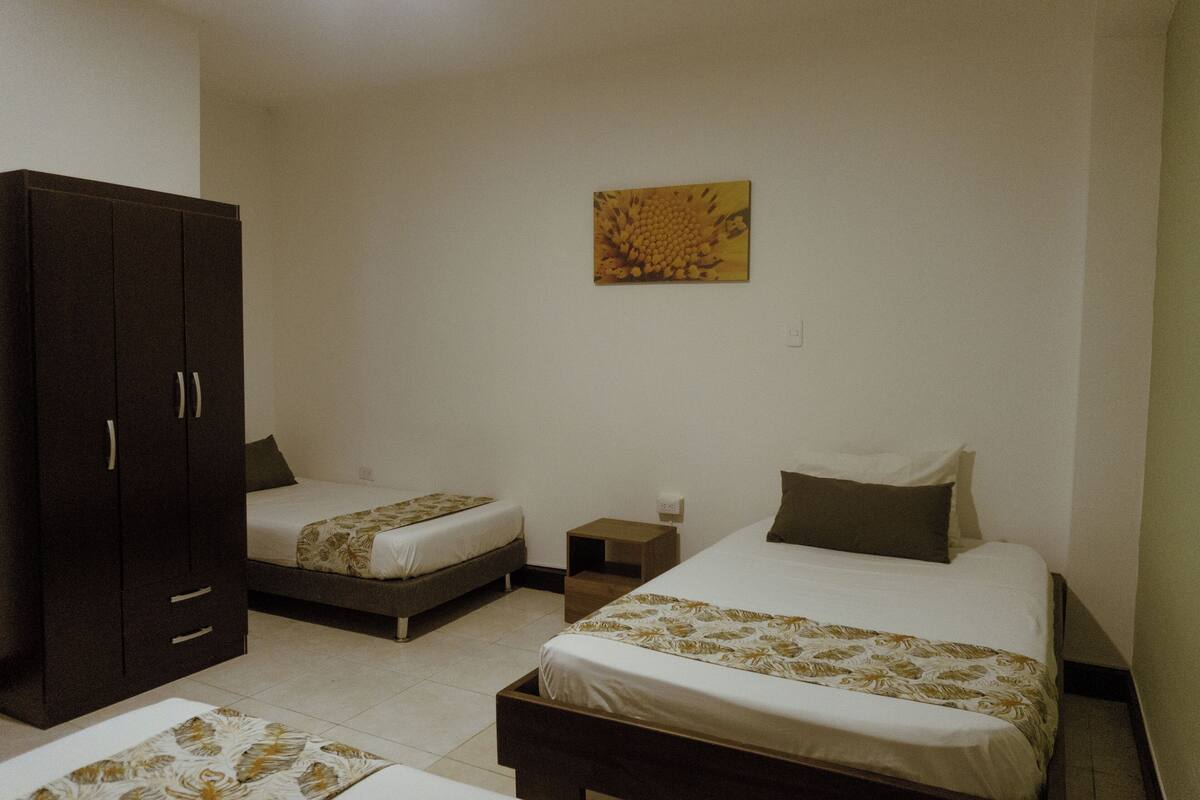 A bedroom with two single beds, a wardrobe, a nightstand, and a wall-mounted artwork.