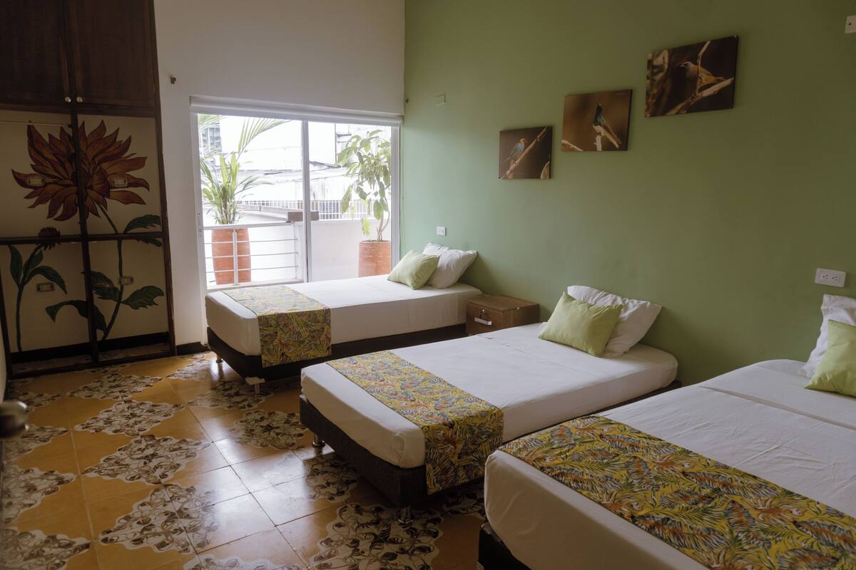 A hotel room with two beds, a large window with a view of the outside, and a green wall with bird paintings.