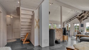 Un intérieur spacieux avec un plafond haut, un escalier menant à une mezzanine et une grande fenêtre qui laisse entrer la lumière naturelle.