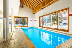 Una piscina interior con vigas de madera, amplias ventanas y vistas a un paisaje nevado.