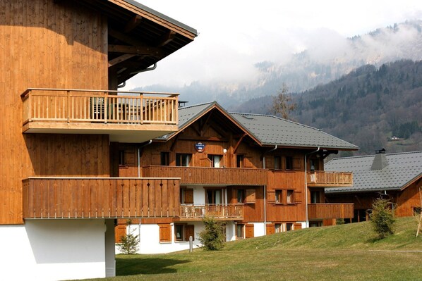 Un chalet de madera con balcones, un cartel que indica 'La Grosse' y un paisaje montañoso al fondo.