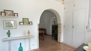 A spacious room with wooden flooring, a white console table with framed artwork, a green bottle, and a green cabinet. - The House on the Knoll-Valle d'Itria CIN:IT073013C200089627 CIS:TA07301391000050432 (Alberobello)