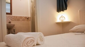 A hotel room with a neatly made bed, a bathroom with a sink and toilet, and a wall-mounted light fixture. - The House on the Knoll-Valle d'Itria CIN:IT073013C200089627 CIS:TA07301391000050432 (Alberobello)