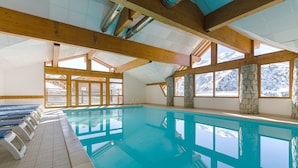 Ein beheiztes Hallenbad mit Holzbalken, Steinwänden und großen Fenstern mit Blick auf die Berge.