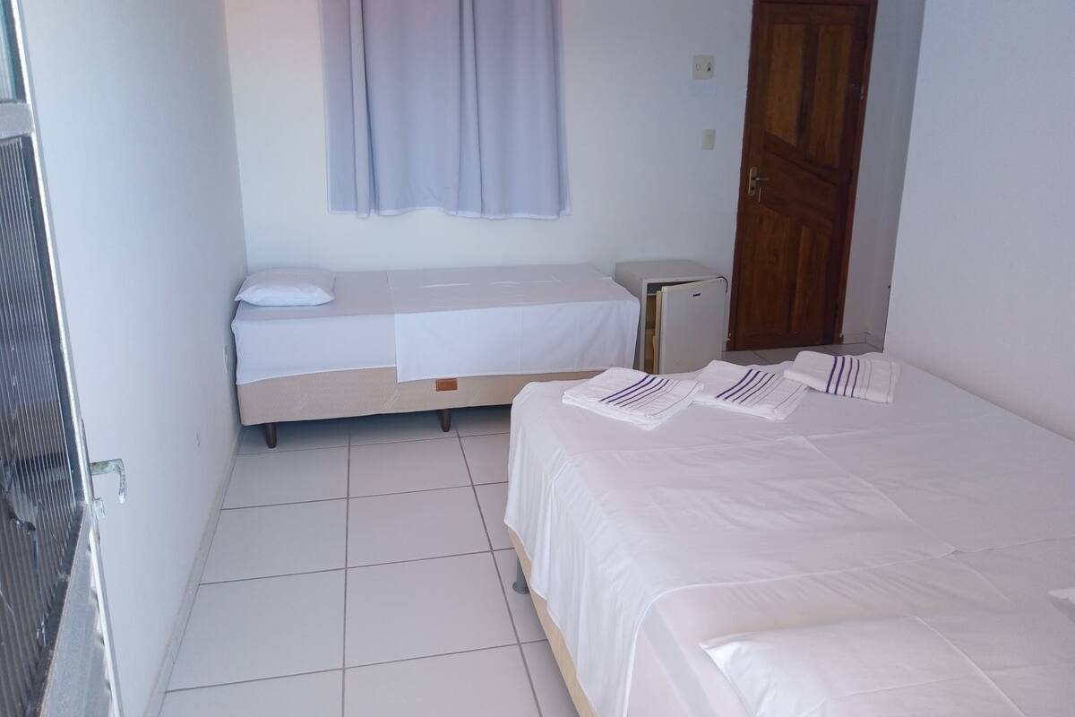 A small, clean room with a bed, a bedside table, a small cabinet, and a door.