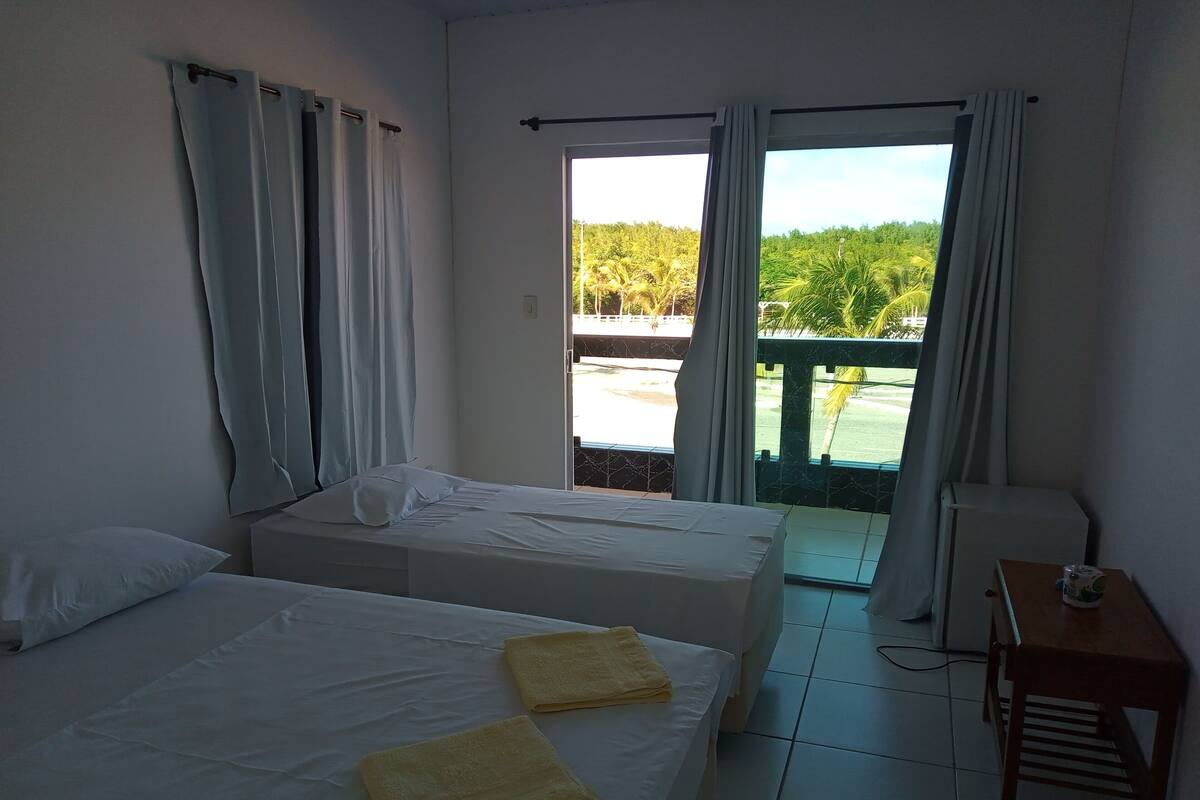 A hotel room with two beds, a small table, and a view of a garden through a sliding door.