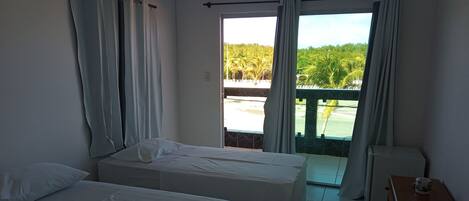 A hotel room with two beds, a small table, and a view of a garden through a sliding door.