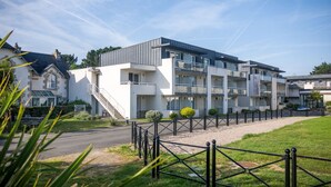 A modern multi-story residential building with a flat roof, large windows, and a gated entrance. - Appartement 300m de la Mer | Accès Piscine (Plougasnou)