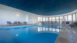 An indoor swimming pool with clear blue water, surrounded by lounge chairs and a tiled floor. - Appartement 300m de la Mer | Accès Piscine (Plougasnou)