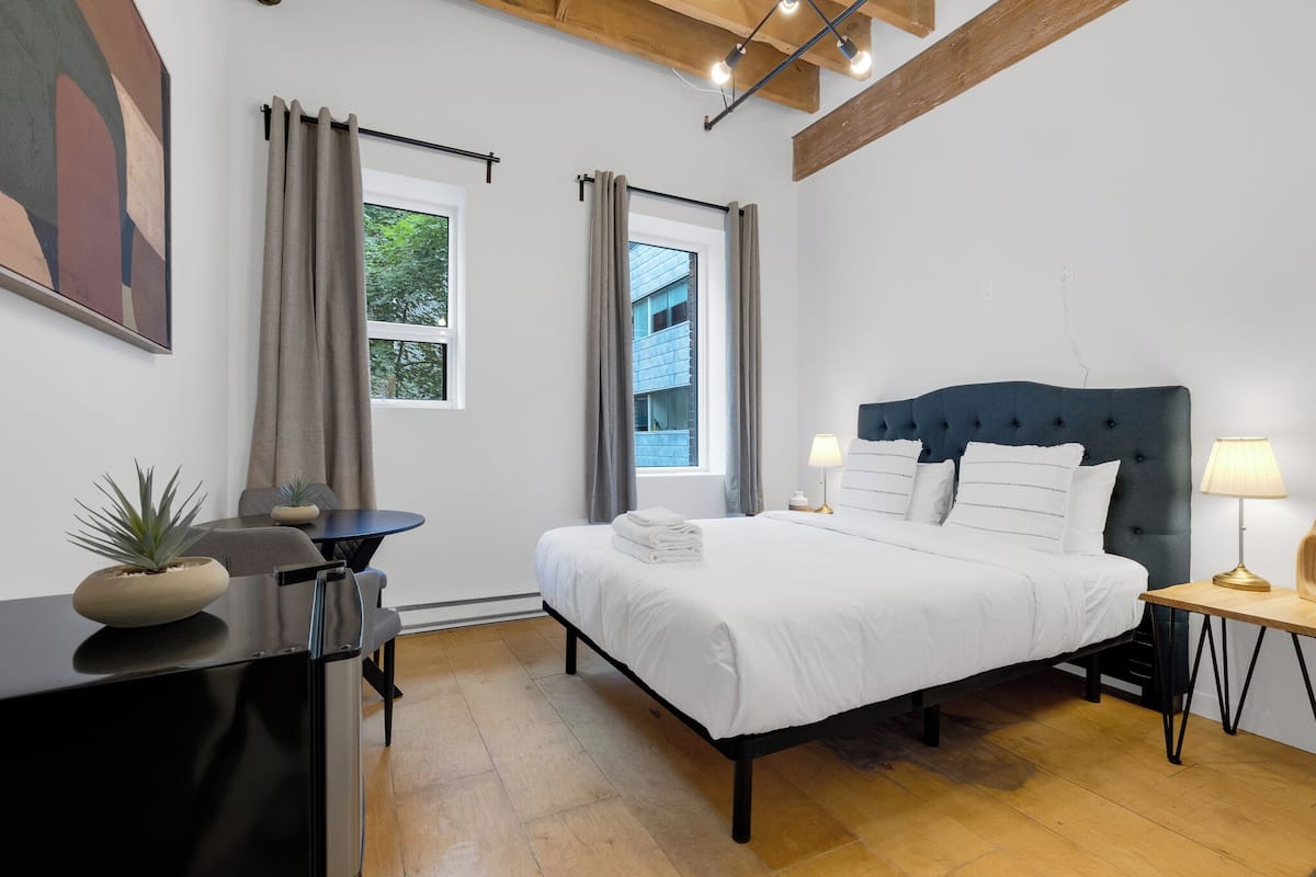 A modern bedroom with a bed, bedside tables, a desk, and a window with curtains.