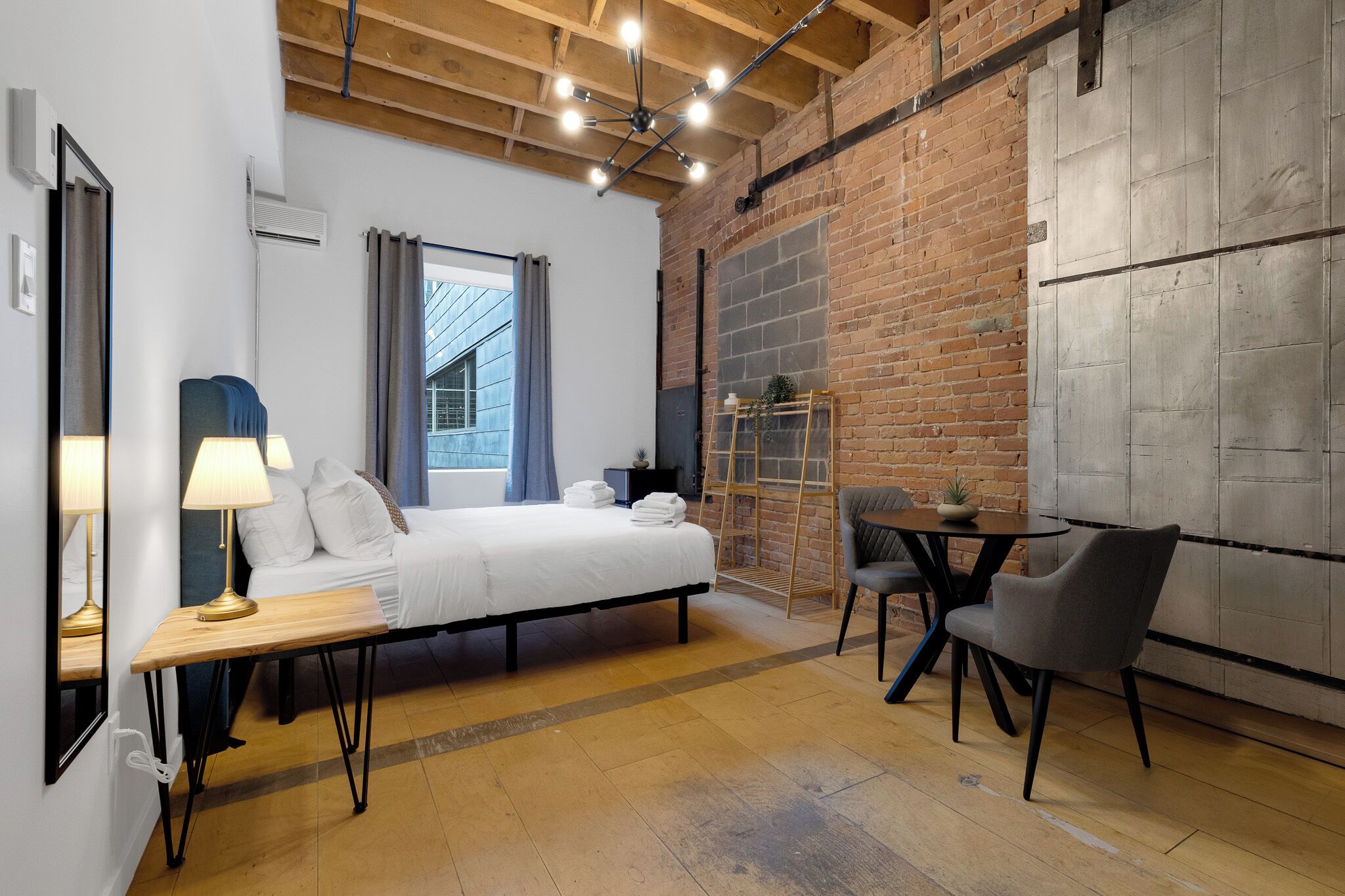 Habitación de hotel moderna con cama, mesita de noche, lámpara, silla y vistas al exterior.
