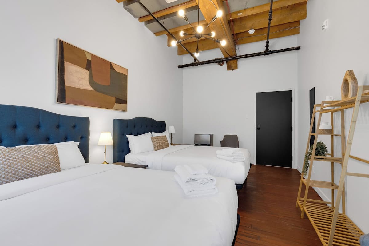 A hotel room with two beds, a large abstract painting, a wooden ladder shelf, and a television.