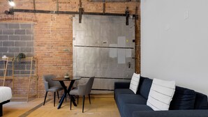 Une pièce chaleureuse avec un mur en briques, une grande porte coulissante, un canapé bleu foncé, une petite table ronde et deux fauteuils gris.